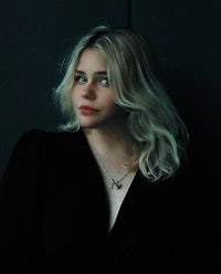 a woman in a black dress leaning against a wall